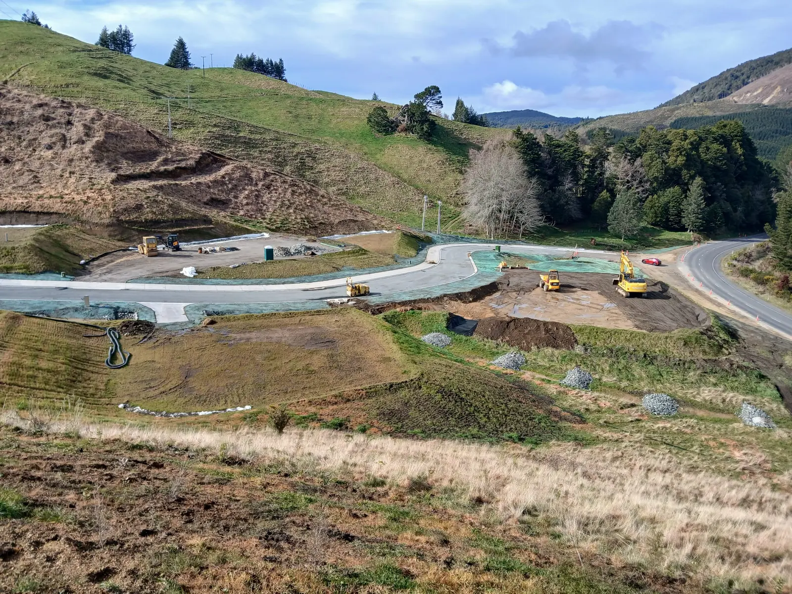 Aerial view of the access road and hydroseeded lot platforms cut into the hillside, with the state highway and forest beyond